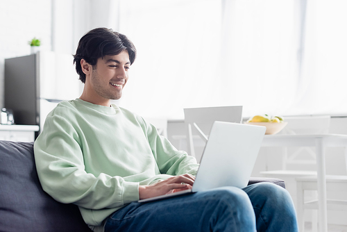 pleased man using laptop while sitting on couch at home