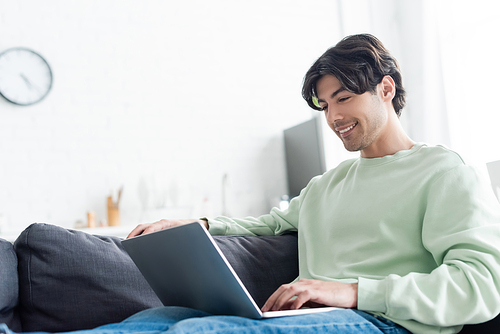 young positive man using laptop on couch at home