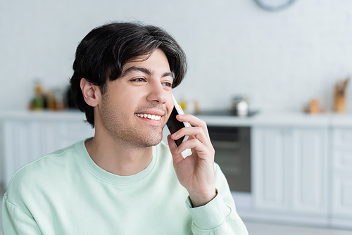 happy young man talking on smartphone in blurred kitchen