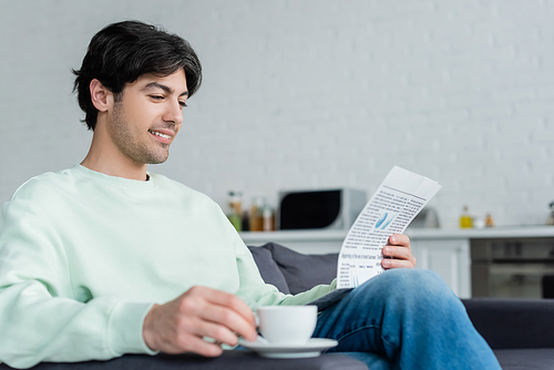 smiling man reading newspaper near blurred coffee cup on sofa