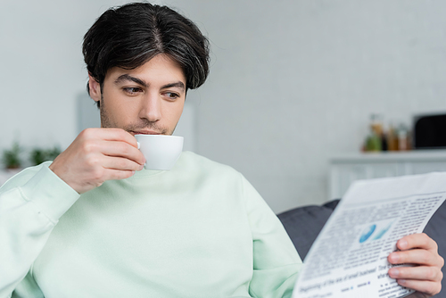 young brunette man drinking coffee and reading newspaper in morning