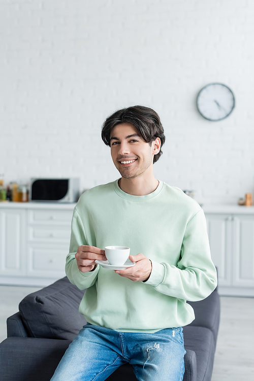 cheerful man with coffee cup  on couch in blurred kitchen