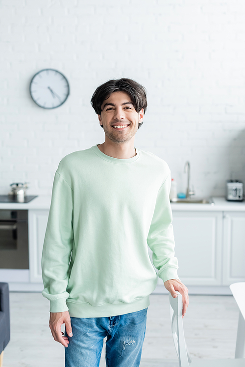 young brunette man smiling at camera while standing in blurred kitchen