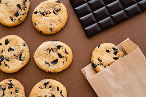 Top view of cookies, paper bag and chocolate bar on brown background