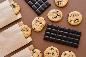 Top view of chocolate bars and cookies in craft packages on brown background