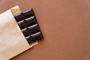 Top view of dark chocolate bar in craft package on brown background