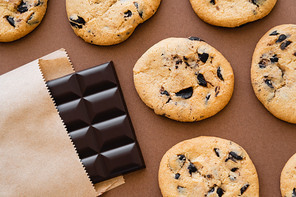 Top view of cookies near chocolate bar in craft package on brown background