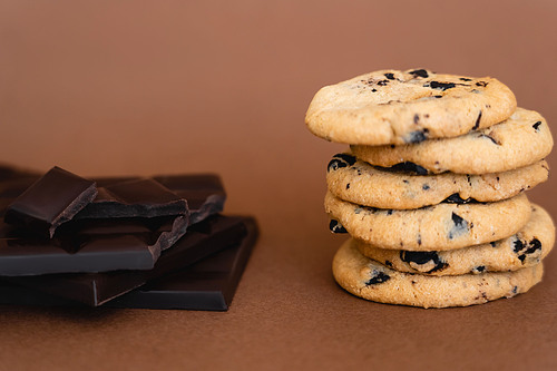 Close up view of cookies and dark chocolate bars on brown background