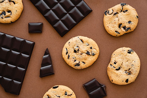 Top view of cookies and dark chocolate on brown background