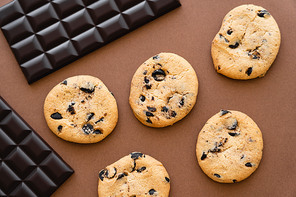 Top view of chocolate bars and cookies on brown background