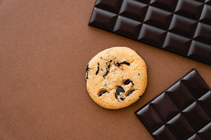 Top view of cookie near dark chocolate bars on brown background