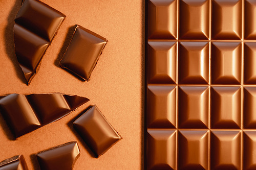 Top view of milk chocolate bar and pieces on brown background