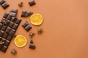 Top view of dark chocolate, dry orange slices and anise spice on brown background