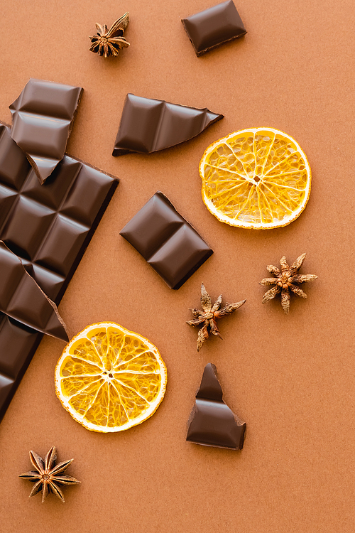 Top view of dry orange slice, chocolate and anise on brown background