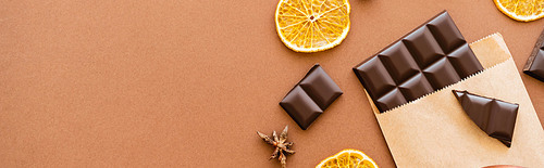 Top view of anise, dry orange slice and chocolate in craft package on brown background, banner