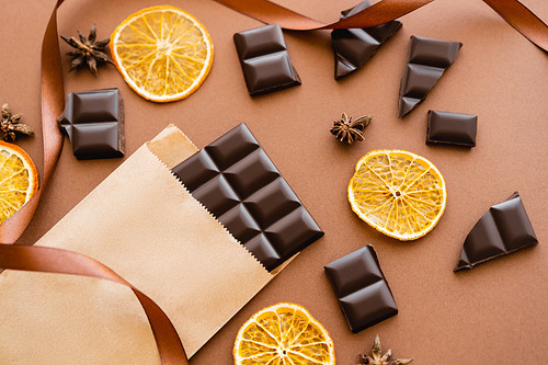 Top view of anise, dry orange slices and chocolate on craft package with ribbon on brown background