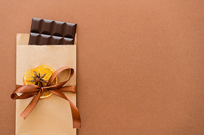 Top view of chocolate in craft package with orange slice and anise on brown background