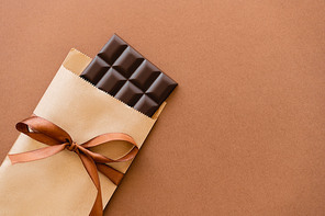 Top view of dark chocolate bar in craft package with ribbon on brown background