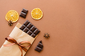 Top view of anise and orange slices near chocolate in craft package with ribbon on brown background