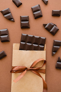 Top view of dark chocolate in craft package with ribbon on brown background