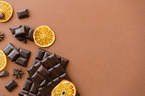 Top view of dark chocolate bars near dry orange slices and anise on brown background