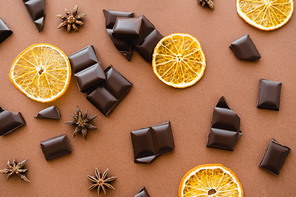 Top view of chocolate pieces, dry orange slices and anise on brown background