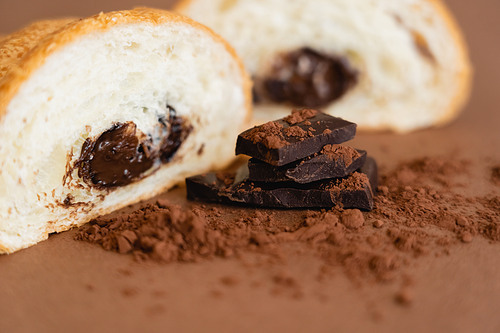 Close up view of croissant near chocolate pieces and cocoa on brown background