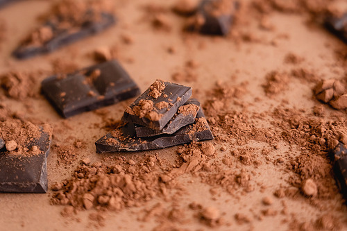 Close up view of cocoa powder on chocolate pieces on brown background