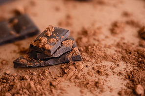 Close up view of natural cocoa powder and chocolate on blurred brown background