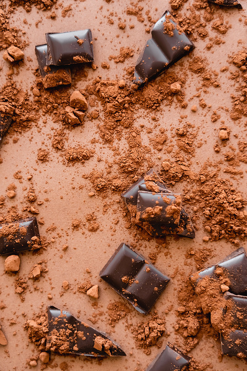 Top view of dry cocoa and dark chocolate pieces on brown background