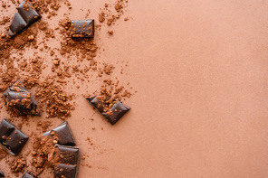 Top view of chocolate pieces and cocoa on brown background with copy space