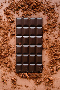 Top view of dark chocolate bar and cocoa on brown background
