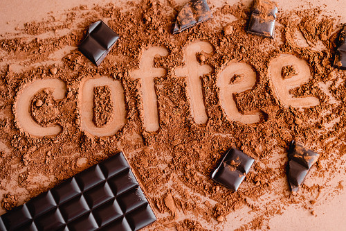 Top view of coffee lettering in cocoa and chocolate on brown background