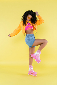 full length of happy and curly african american young woman in pink roller skates on yellow