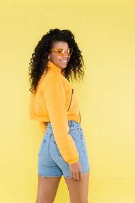 happy african american young woman in sunglasses isolated on yellow