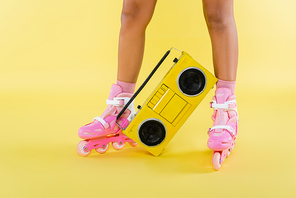 cropped view of african american woman in roller skates near retro boombox on yellow