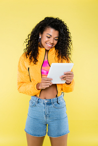 positive african american young woman using digital tablet isolated on yellow