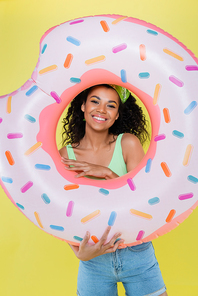 happy african american young woman holding inflatable ring isolated on yellow
