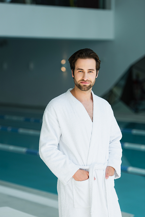 Young man holding hands in pockets of bathrobe in spa center