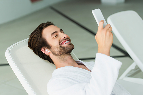 Smiling man in earphone using smartphone in spa center