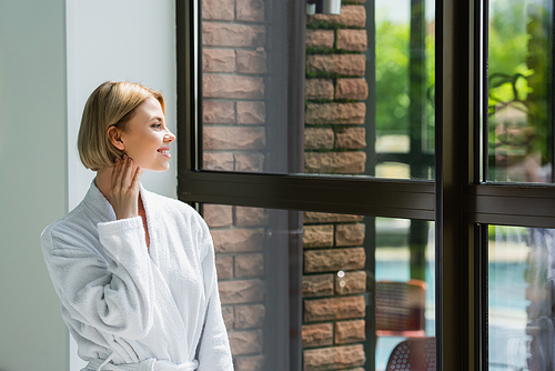 Side view of woman in white bathrobe looking at window in spa center