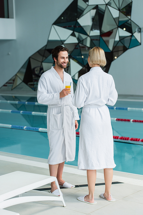 Cheerful man with orange juice talking with girlfriend in spa center