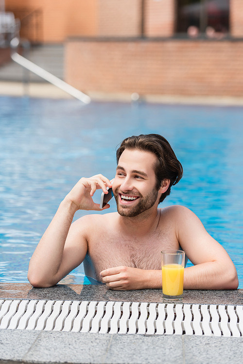Happy man talking on smartphone near orange juice in swimming pool