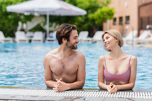 Young couple smiling at each other in swimming pool on resort