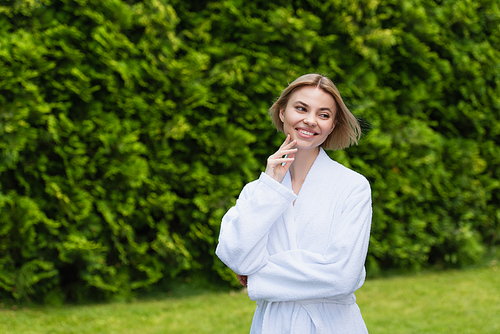 Positive woman in white bathrobe looking away on resort outdoors
