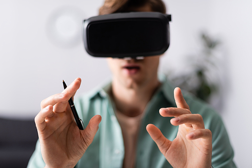 Selective focus of man in vr headset holding pen at home