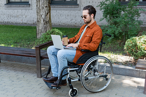 handicapped man with takeaway drink sitting in wheelchair and working on laptop
