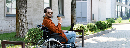 disabled man in sunglasses holding coffee to go while sitting in wheelchair with laptop, banner
