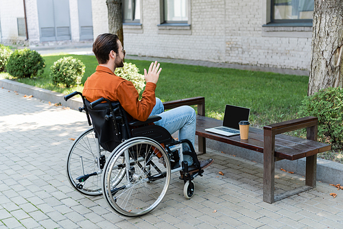 handicapped man in wheelchair waving hand during video chat on laptop outdoors