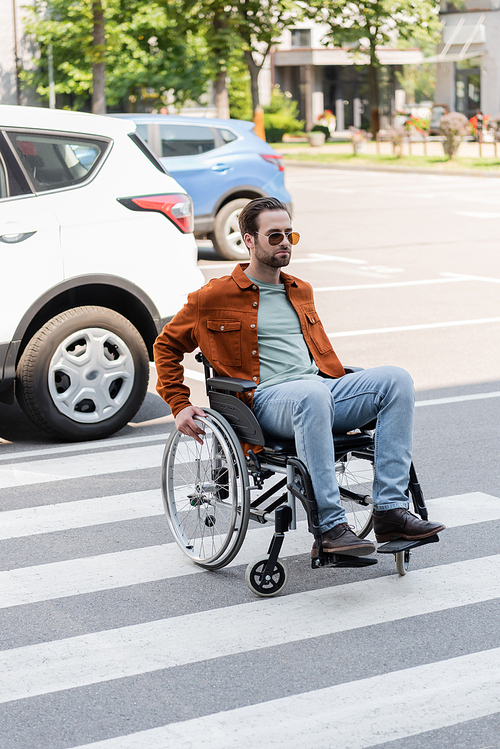 disabled man in wheelchair crossing road near cars in city